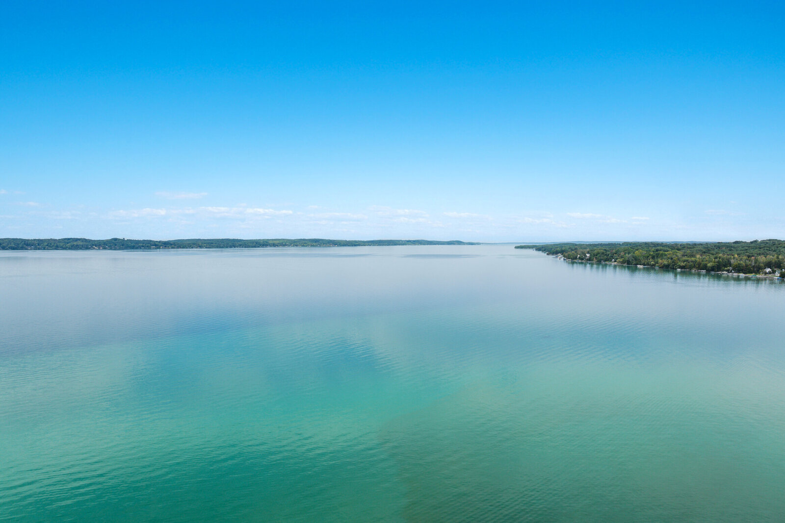Torch Lake's turquoise shallows meeting blue water and a wooded shoreline